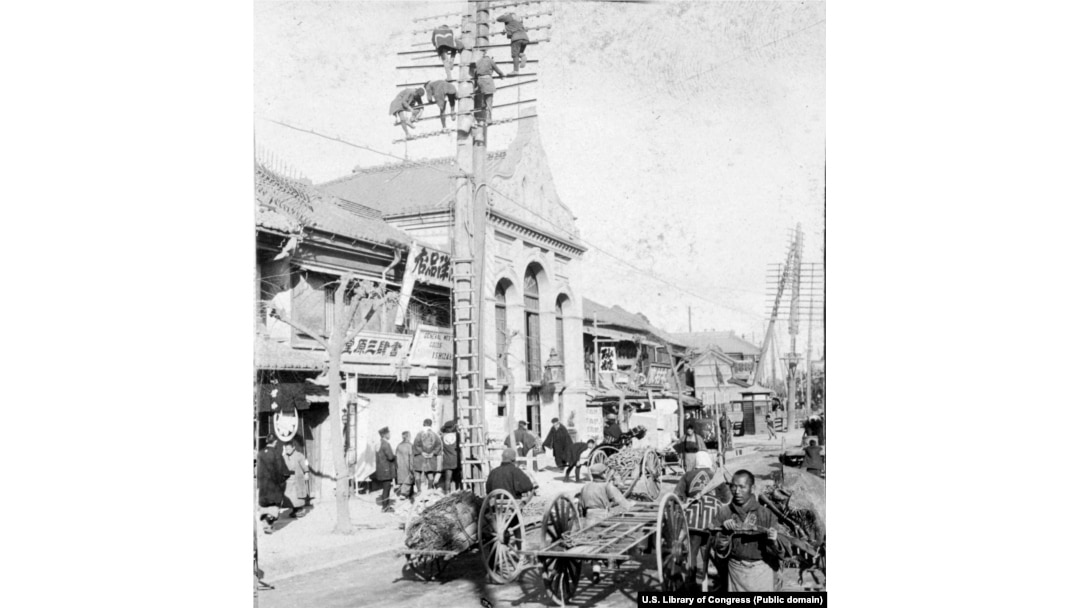 Рабочие устанавливают телеграфные столбы над оживленной улицей Токио, 1905 год
