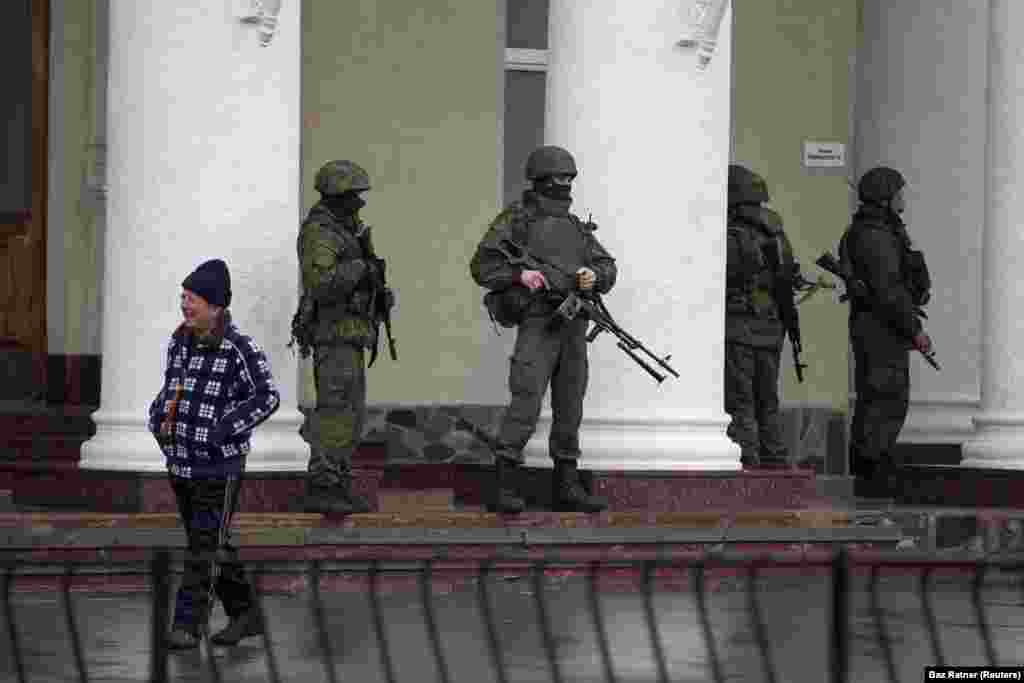 Российские солдаты, действующие без знаков различия, стоят возле аэропорта Симферополя, 28 февраля 2014 года. Российские солдаты-инкогнито появились по всему Крыму и стали известны как «зеленые человечки». Кремль первоначально утверждал, что это были местные группы «самообороны», но позже признал, что это были профессиональные российские солдаты.