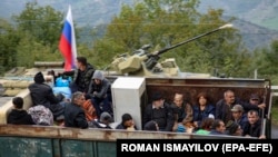 A truck carrying ethnic Armenians fleeing Karabakh drives past a Russian armored vehicle in the Lachin corridor, September 26, 2023.