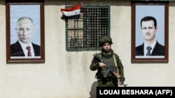 Un soldat rus stă între portretele președintelui sirian Bashar al-Assad (d) și cel rus, Vladimir Putin, la un punct de control de lângă Damasc, în 2018.