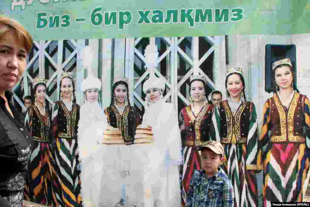 Қазақ және өзбек ұлттық костюмдерін киген қыздар суретінің жанында тұрған әйел мен бала. 