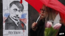 Not the first time: A woman walks in front of a poster in Kyiv on March 3 depicting Russian President Vladimir Putin as Adolf Hitler and signed "Hands off Ukraine."