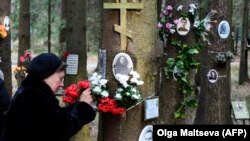A woman fastens flowers to a tree with portraits of victims of Soviet dictator Joseph Stalin's purges at the memorial where the victims were buried in the woods on the outskirts of St. Petersburg, on October 30.