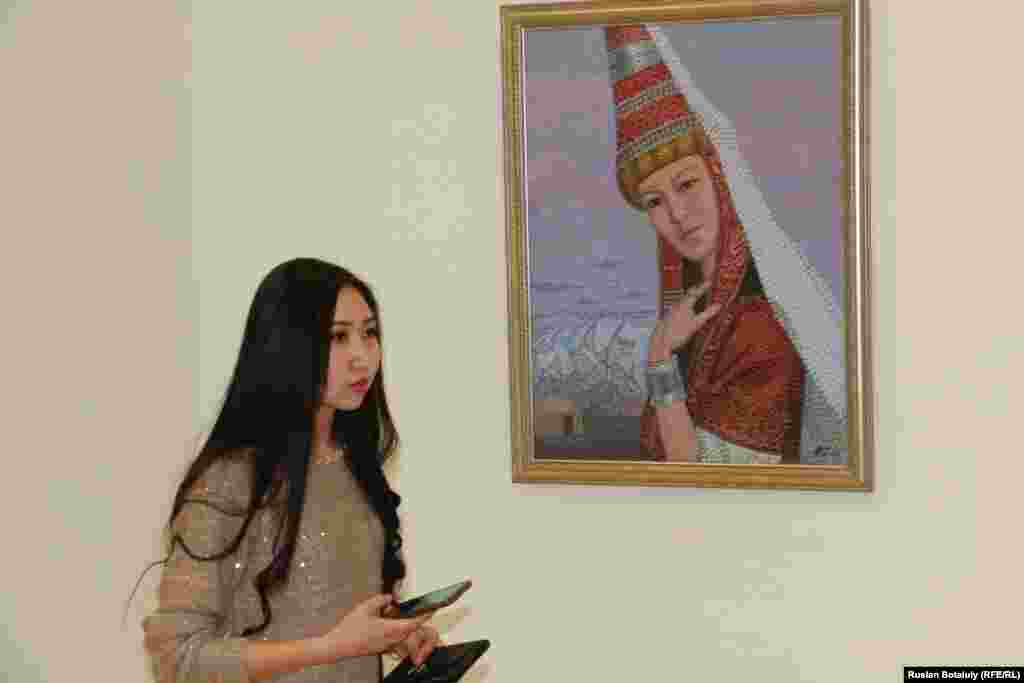 Рядом с картиной, где изображена девушка в казахской национальной праздничной одежде. 