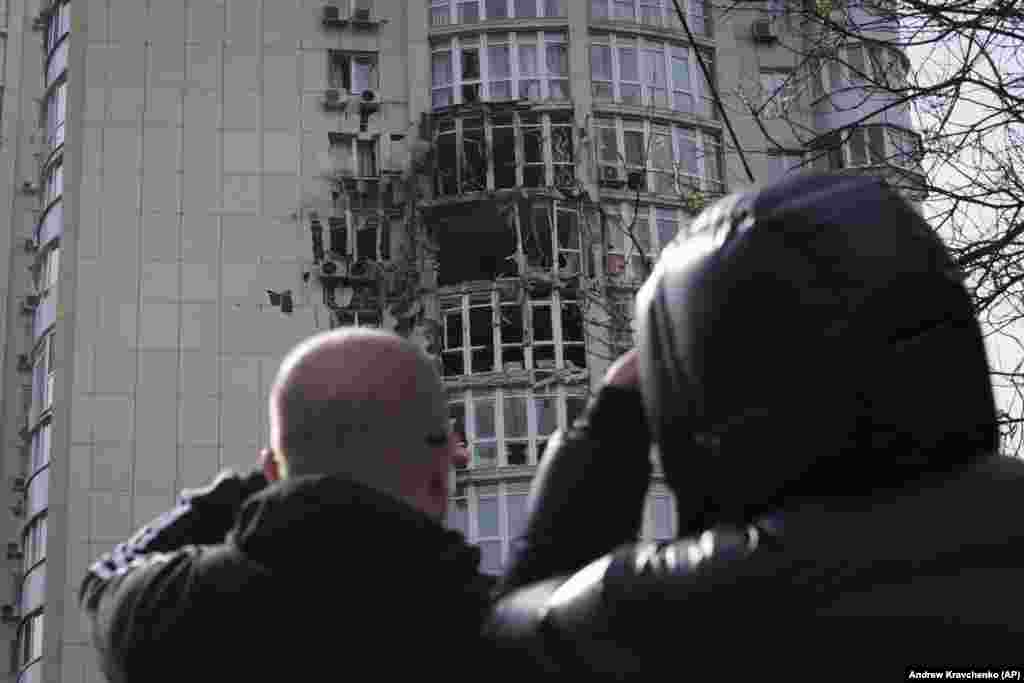 Люди смотрят на многоквартирный дом, повреждённый беспилотником, сбитым во время ночного удара России по Киеву