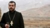 Iran -- An Armenian priest prays on the Iranian-Azerbaijani border against the backdrop of Azerbaijani soldiers destroying Armenian cross stones at the Djulfa cemetery, December 2005. (Photo couresty of Djulfa.com)