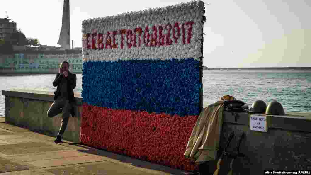 Чоловік чекає туристів, щоб сфотографувати на тлі триколора «Севастополь»